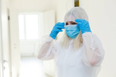 Asyalı kadın koruyucu bir maske ve takım elbise giyer. Grip, ebola, tüberküloz ve virüsten korunuyor. Biyolojik tehlikeye karşı kişisel koruma ekipmanları.