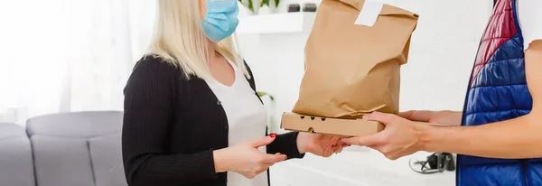宅配男から小包を受け取った医療マスクを身に着けている若い女性が屋内 ウイルスの拡散防止 — ストック写真