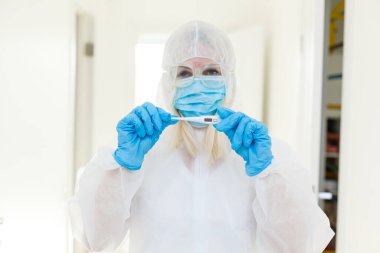 Tehlikeli madde koruma giysisi içindeki araştırmacı kimya laboratuarındaki bir deney tüpünü inceliyor..