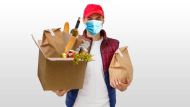 Elinde beyaz arka planda yiyecek olan kağıt torba taşıyan teslimatçı. Koruyucu maskeli yemek dağıtan adam.