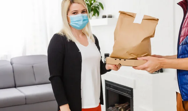 戴着医疗面罩的年轻妇女在室内接受送货男子送来的包裹 防止病毒传播 — 图库照片