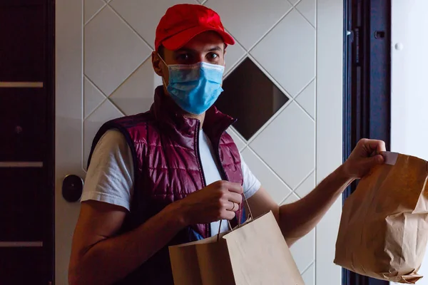 Delivery man holding paper bag with food on white background, food delivery man in protective mask