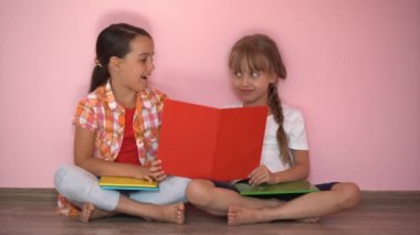 Pembe arka planda kitap okuyan iki küçük kız.