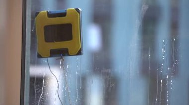 Modern robotik pencere temizleyicisi iş başında. Elektrikli süpürge robotu apartmanın penceresini temizliyor. Ev hizmeti ve temizlik konsepti. 4k video