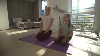 Narin bir anne ve güzel küçük kızı evdeki minderde yoga yapıyorlar, Front View.
