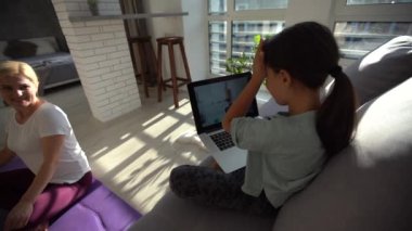 Alıştırma elbiseli çekici bir kadın evde halıda antrenman yapıyor ve küçük komik bir kız çocuğu yanında oturuyor.