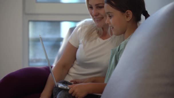 행복 한 엄마와 귀여운 딸이 집에서 학습용 노트북을 사용하며 즐겁게 이야기하고, 미소짓고 있으며, 엄마가 온라인 쇼핑을 가르치고 있고, 웹캠은 컴퓨터 화면을 보며 소파에 앉아 있습니다. — 비디오
