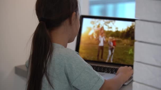 En söt liten flicka som tittar igenom familjefoton på laptop. Underhållning, fritid och utbildning för barn med hjälp av modern teknik. — Stockvideo