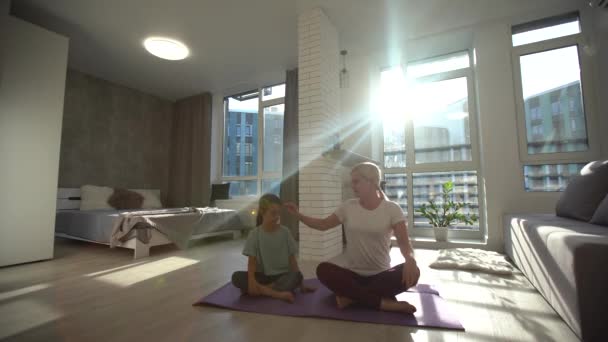 YOGA: Slender mom with her pretty little daughter practising yoga on a mat at home - Front View — Stock Video