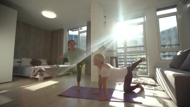Feliz familia saludable hija y madre joven divirtiéndose haciendo ejercicios de yoga juntos, mamá sonriente y consciente enseñando a la niña linda a meditar riendo en casa — Vídeo de stock