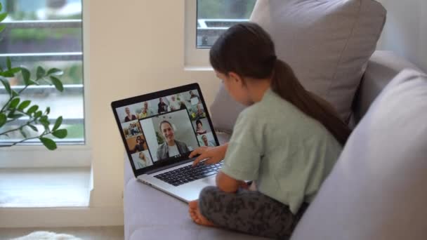 Het meisje in de koptelefoon kijkt met interesse naar het laptopscherm en zwaait hallo. afstandsonderwijs, school online. — Stockvideo