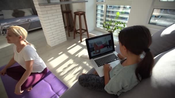 Charmig stark fitness kvinna i träningskläder gör träning på matta hemma och liten rolig dotter sitter nära henne — Stockvideo