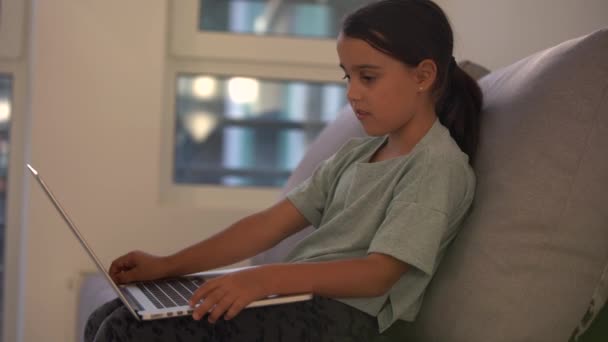 Het meisje in de koptelefoon kijkt met interesse naar het laptopscherm en zwaait hallo. afstandsonderwijs, school online. — Stockvideo