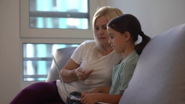 Mãe feliz e filha criança bonito se divertindo conversando usando laptop de aprendizagem em casa, mãe sorridente ensinar criança pequena compras on-line fazer videochamada webcam olhando para a tela do computador sentar no sofá — Vídeo de Stock