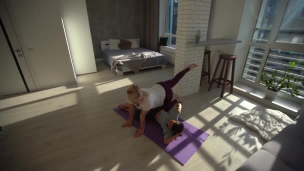 Narin bir anne ve güzel küçük kızı evdeki minderde yoga yapıyorlar, Front View. — Stok video