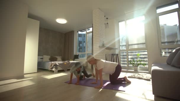Feliz familia saludable hija y madre joven divirtiéndose haciendo ejercicios de yoga juntos, mamá sonriente y consciente enseñando a la niña linda a meditar riendo en casa — Vídeos de Stock