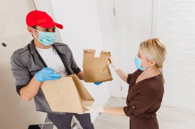 Elinde beyaz arka planda yiyecek olan kağıt torba taşıyan teslimatçı. Koruyucu maskeli yemek dağıtan adam.