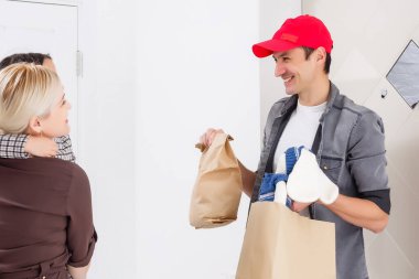 Gülümseyen genç kadın ve kızı evdeki teslimatçıdan yemek alıyorlar..