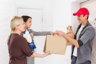 Gülümseyen genç kadın ve kızı evdeki teslimatçıdan yemek alıyorlar..