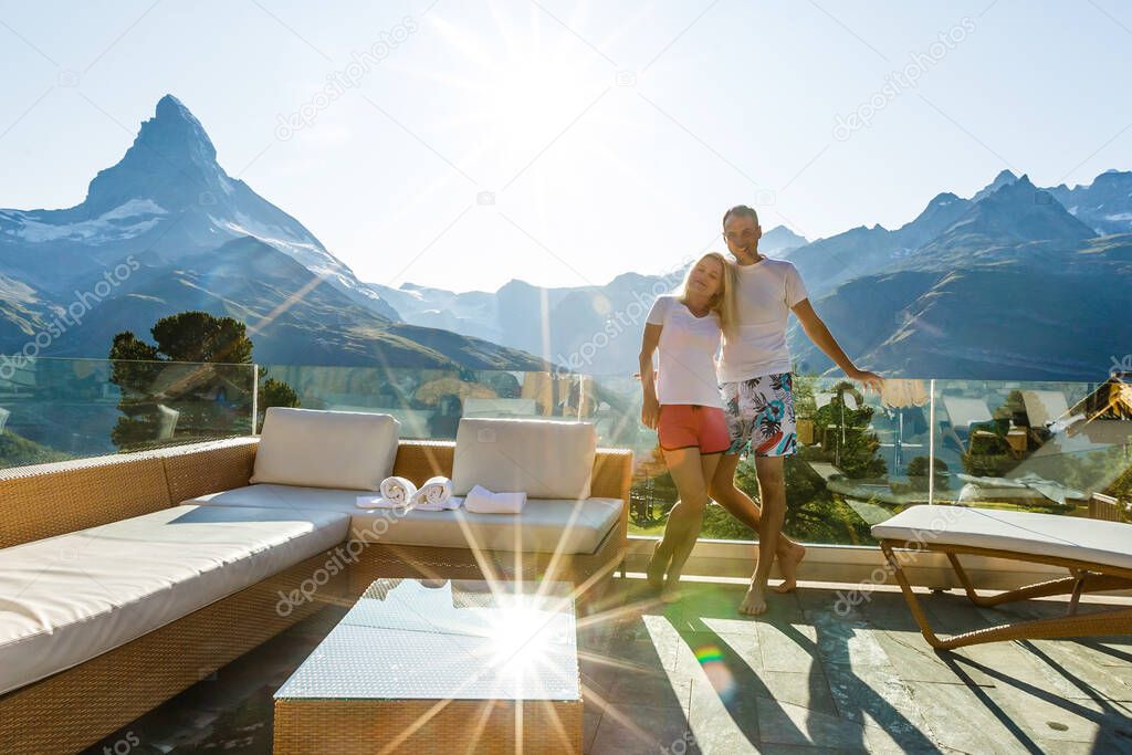 Young couple - man and woman relaxing on terrace of wooden house in mountains. Romantic morning of two lovers.