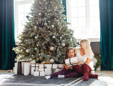 Mutlu aile annesi ve kızı Noel hediyesiyle Noel ağacının yanında.