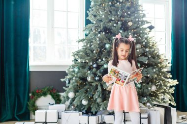 Küçük kız Noel ağacının önünde fotobook gibi görünüyor.