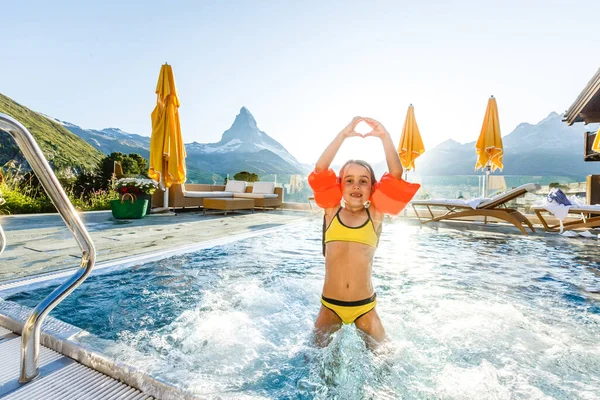 Little girl playing in outdoor swimming pool of luxury spa alpine resort in Alps mountains, Austria. Winter and snow vacation with kids. Hot tub outdoors with mountain view. Children play and swim.