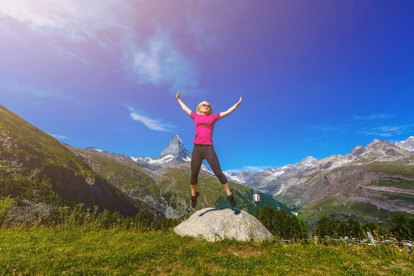 Young girl holds hands up against the sky and mountain