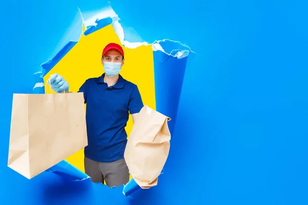青い背景に隔離された食品と均一なホールドクラフト紙パケットの配達人 宅配便として働くキャップTシャツの男性従業員 サービスコンセプト モックアップコピースペース — ストック写真