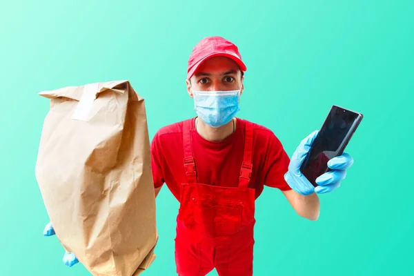 Delivery man in cap k t-shirt uniform face mask gloves hold cardboard box isolated on color background. Service quarantine pandemic coronavirus virus 2019-ncov concept