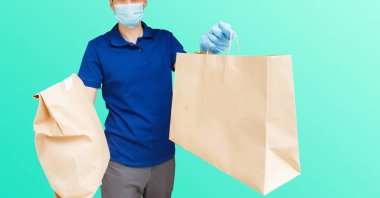 Maskeli ve eldivenli teslimatçı müşterinin evine taze yiyecek getiriyor. Evde kal. İnternetten alışveriş konsepti. mavi arkaplan