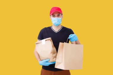 Maskeli ve eldivenli teslimatçı müşterinin evine taze yiyecek getiriyor. Evde kal. İnternetten alışveriş konsepti. sarı arkaplan