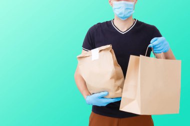 Maskeli ve eldivenli teslimatçı müşterinin evine taze yiyecek getiriyor. Evde kal. İnternetten alışveriş konsepti. yeşil arkaplan
