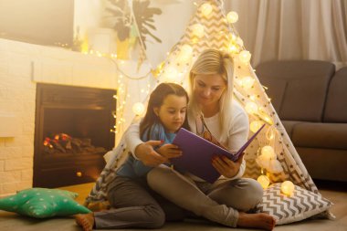 Çocuk kitabı okuyan ve şöminenin başında dinlenen bir anne. Soğuk bir akşam, kış hafta sonları, rahat bir sahne.