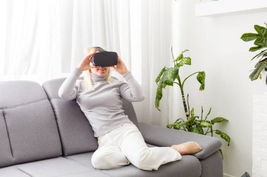 Gelecek şu andır. Çekici genç bir kadın, VR kulaklığını ayarlıyor ve evde otururken gülümsüyor.