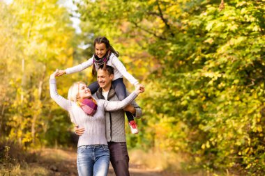 Mutlu aile güz parkında arka planda bulanık yapraklarla eğleniyor.