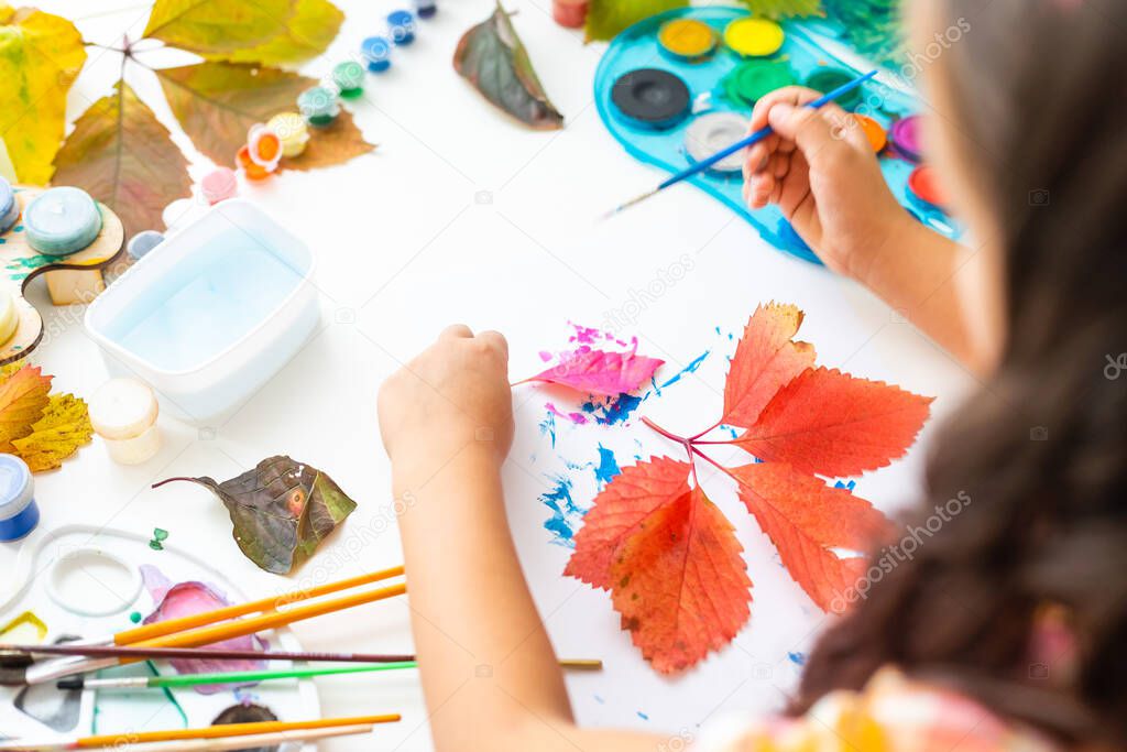 little girl paints leaves with brush at home, autumn art.