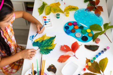 Küçük kız evde sonbahar yapraklarını renklendiriyor