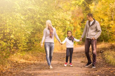 Mutlu aile güz parkında arka planda bulanık yapraklarla eğleniyor.