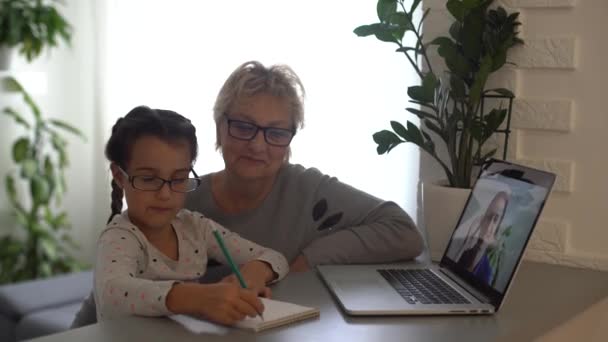 小女孩在家里和奶奶一起学习，用笔记本电脑上学，上网学习，在家学习。女孩在远程学习中有家庭作业。家庭检疫系数-19的生活方式概念. — 图库视频影像