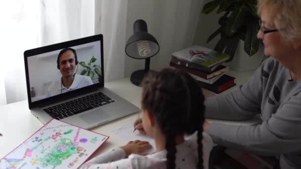 Aprendizaje a distancia de niñas de escuela primaria bastante en casa. Niño lindo enfocado escuchando lecciones de audio estudiando en la mesa, haciendo la tarea. Educación a distancia para niños sobre el concepto de cuarentena. — Vídeo de stock