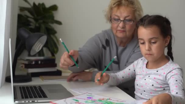 Маленькая девочка учится со своей бабушкой дома, использовать ноутбук для образования, онлайн исследования, домашнее обучение. У девочки домашнее задание на дистанционном обучении. Концепция образа жизни для семейного карантинного ковида-19. — стоковое видео