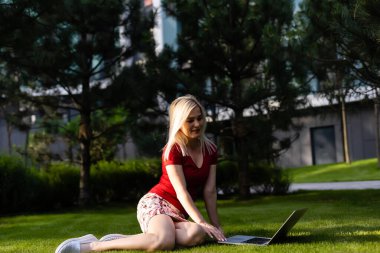 Parkta dizüstü bilgisayar kullanarak gülümseyen genç kadın.