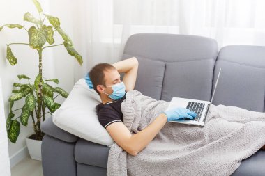 Koruyucu maske takan adam yatakta yatıyor ve evde dizüstü bilgisayarla çalışıyor. Çin 'den yeni Coronavirus 2019-nCoV