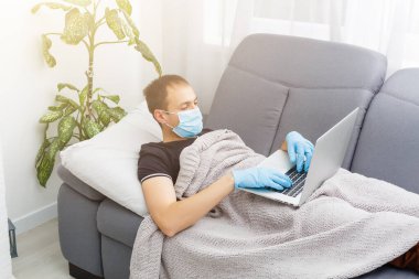 Koruyucu maske takan adam yatakta yatıyor ve evde dizüstü bilgisayarla çalışıyor. Çin 'den yeni Coronavirus 2019-nCoV