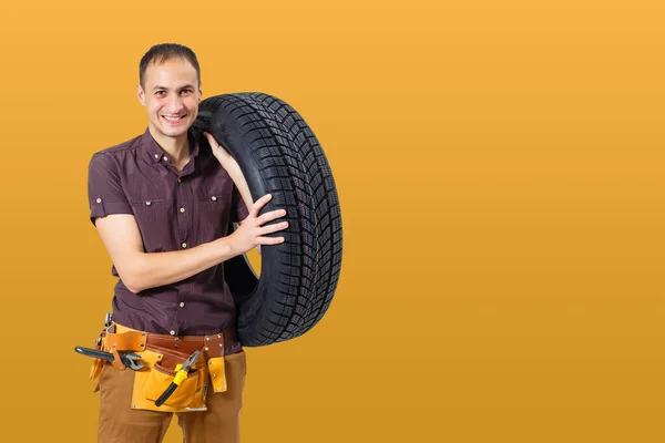 带着黄色底轮胎的汽车修理工 快乐的男人微笑着看着摄像机 — 图库照片