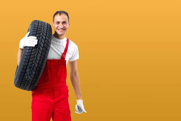 带着黄色底轮胎的汽车修理工 快乐的男人微笑着看着摄像机 — 图库照片