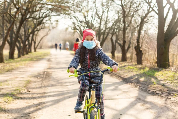 Little girl wearing medical mask prevent flu, pollutions and covid-19 riding bicycle outdoor.