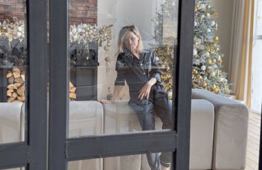 Siyah pijamalı sarışın kadın Noel ağacının yanında oturuyor ve poz veriyor. Yüksek kalite fotoğraf