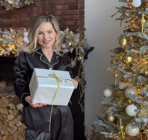  Mutlu romantik kadın Noel ağacının arkasında duruyor. Hediye kutusundaki açılıştan sonra neşeli bayan hediyeyi görünce şaşırdı. Mutlu Noeller ve mutlu tatiller. Yüksek kalite fotoğraf